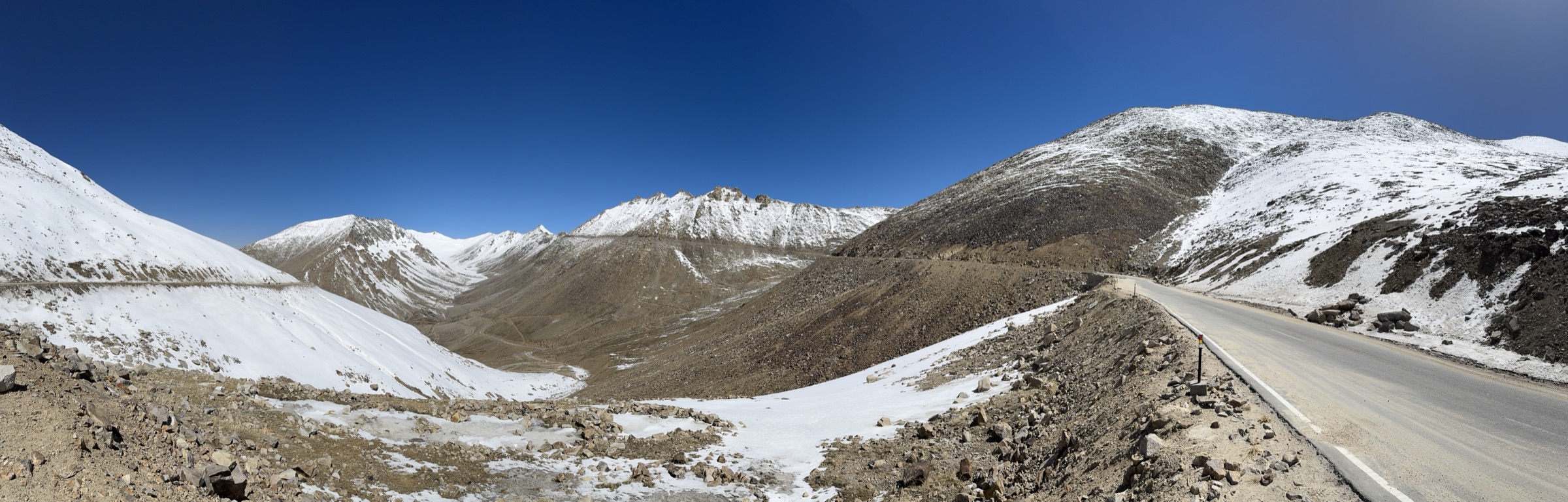 Panoramic view of snow-capped Himalayan peaks near Khardung La, with a mountain road winding through the white landscape
