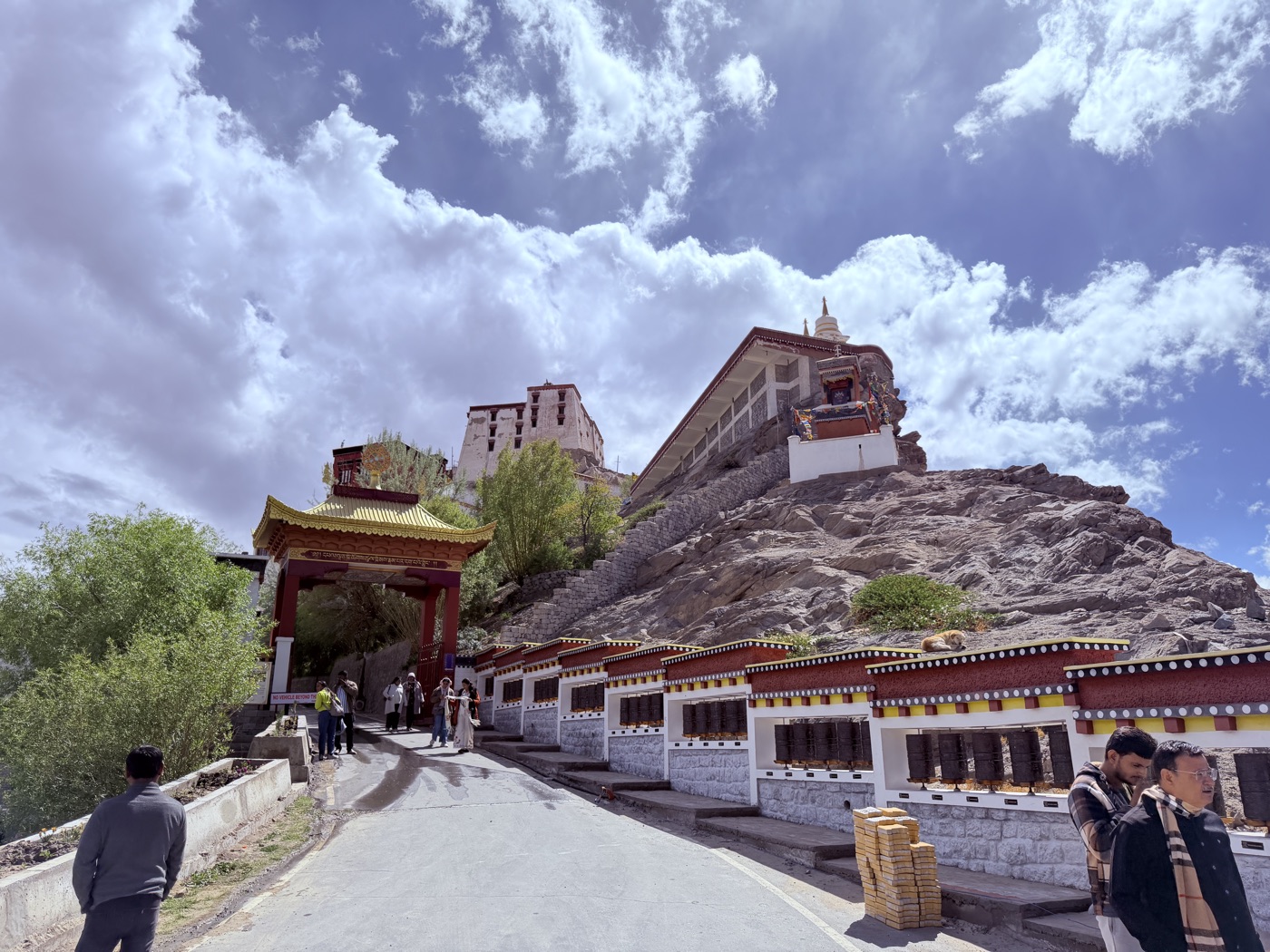 Path ascending to a Ladakhi monastery, flanked by rows of prayer wheels beneath a deep blue Himalayan sky