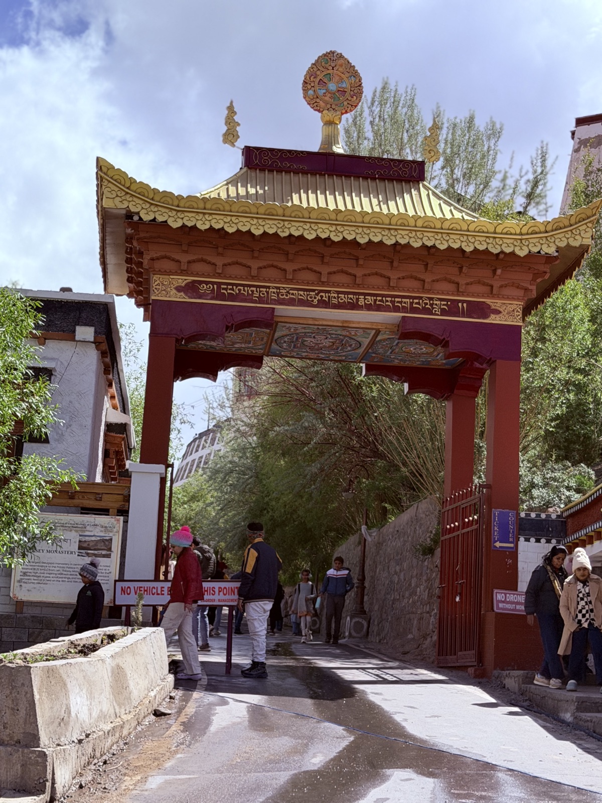 Ornate Tibetan Buddhist gateway with gold finial and intricate painted Dharma wheel, marking the entrance to a Ladakhi monastery