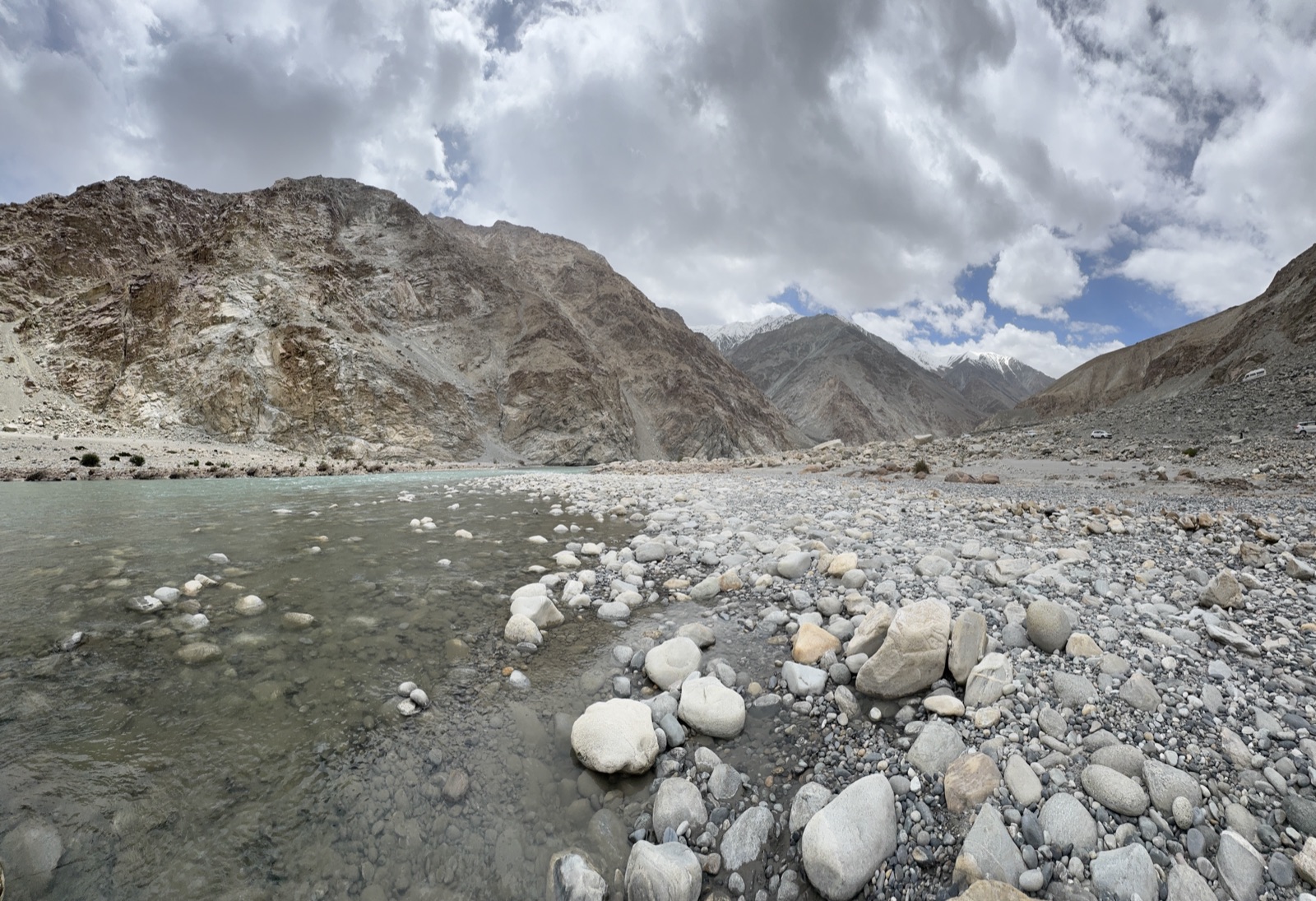 Turquoise glacial river flowing through a dramatic high-altitude rocky gorge, white boulders in the foreground
