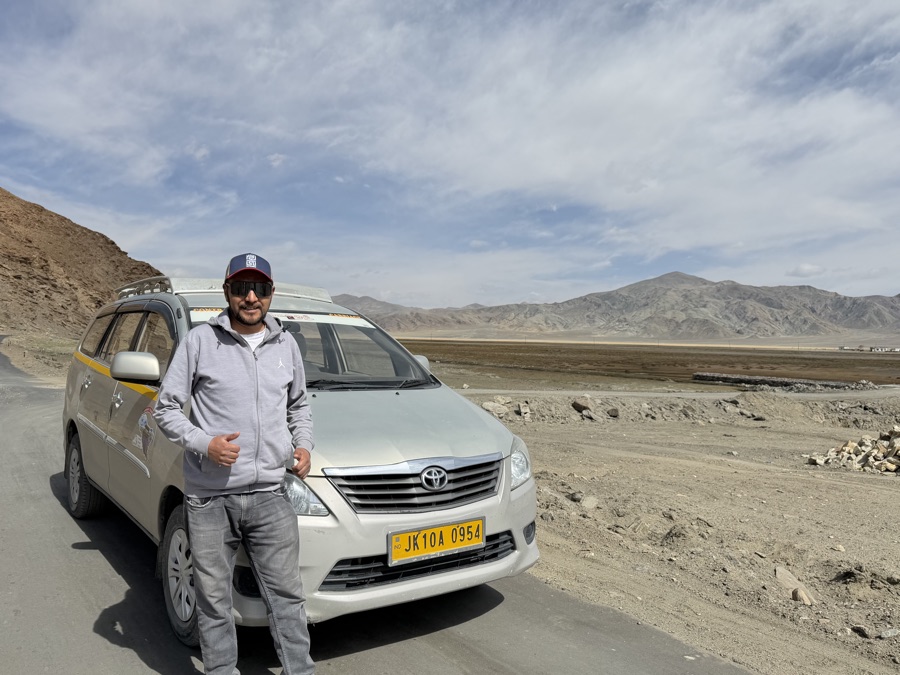 Nazir Hussain standing beside his Toyota Innova Crysta on a Ladakh mountain road